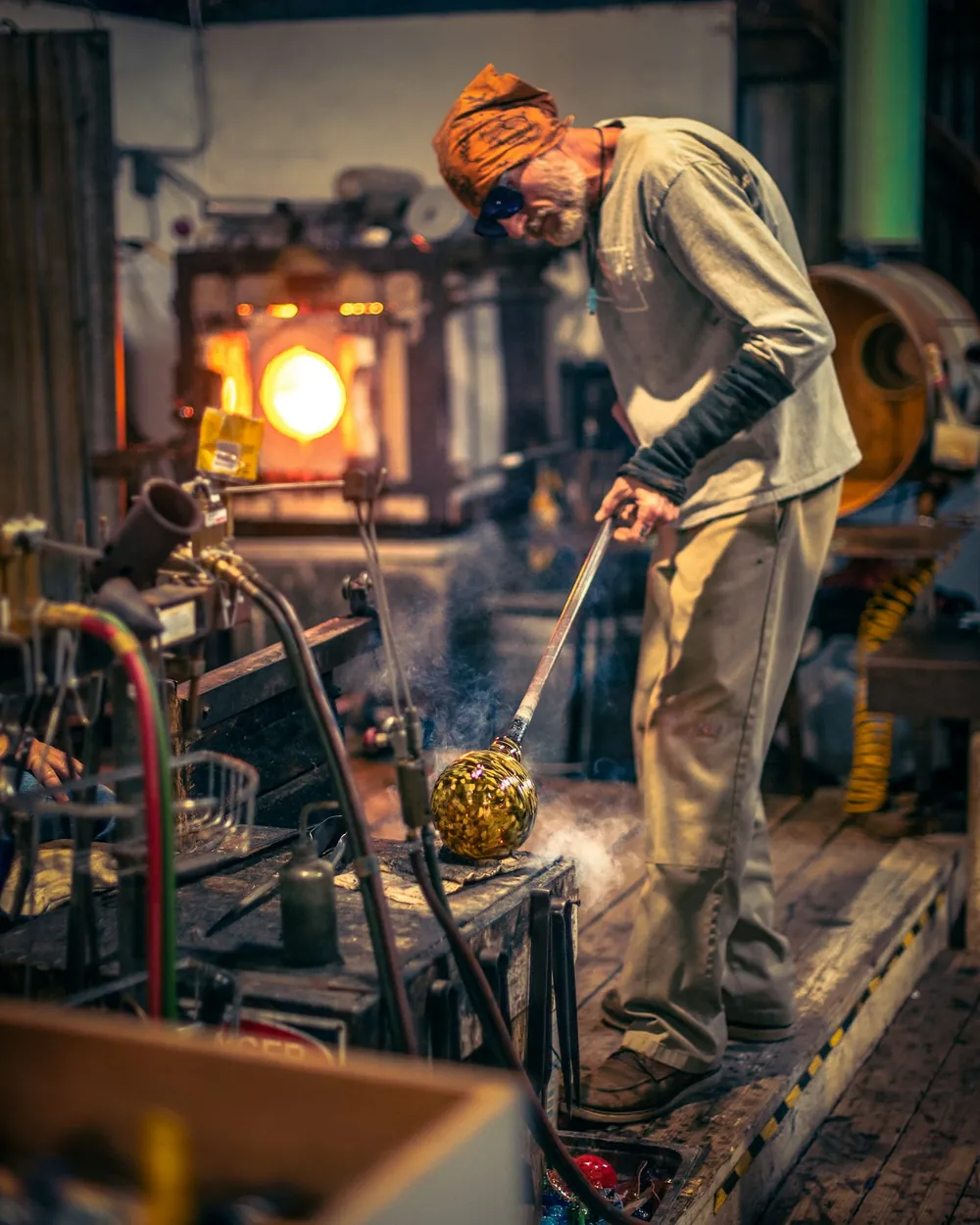Vidriero recogiendo vidrio fundido con la caña frente a la boca encendida del horno de un taller